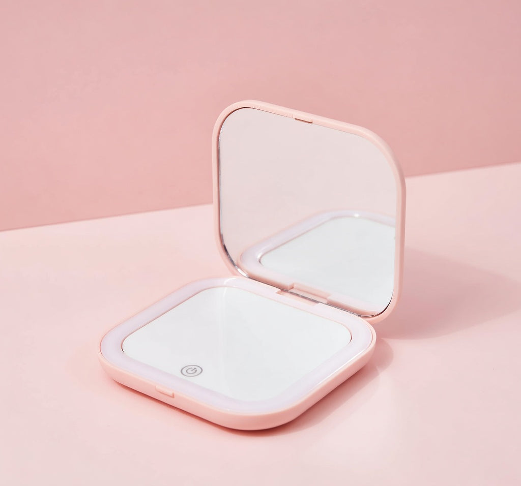 Pink compact mirror with open lid on a pink background.