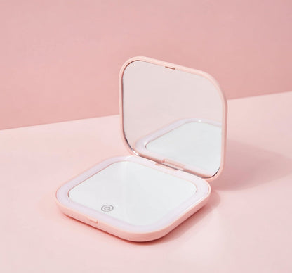 Pink compact mirror with open lid on a pink background.